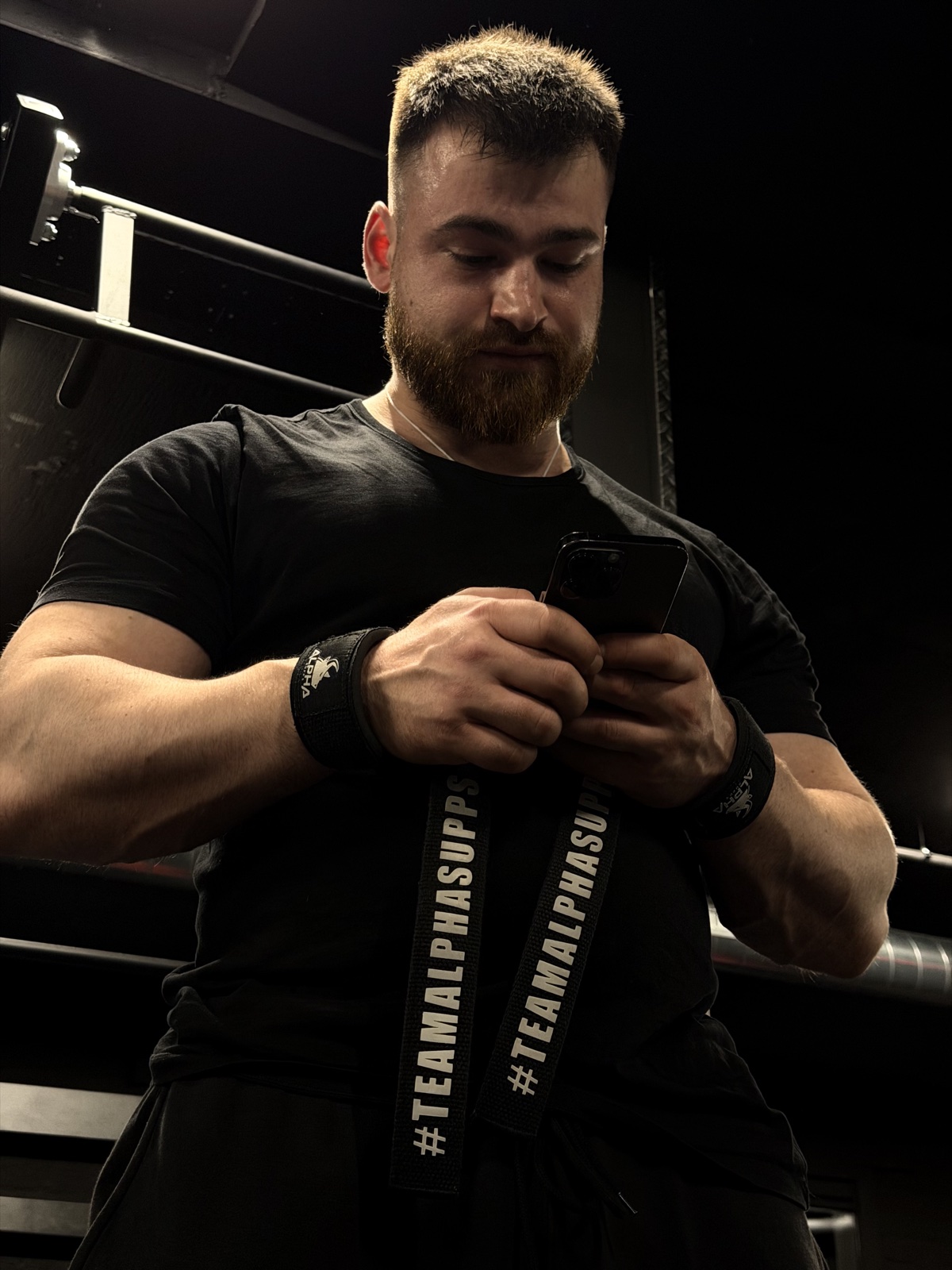 Artjom in the gym with lifting straps, checking his phone